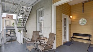 A covered porch with wicker chairs and a bench, a staircase, and a door leading to a building. - Charming Historic Apartment, Heated Pool Access (Savannah)