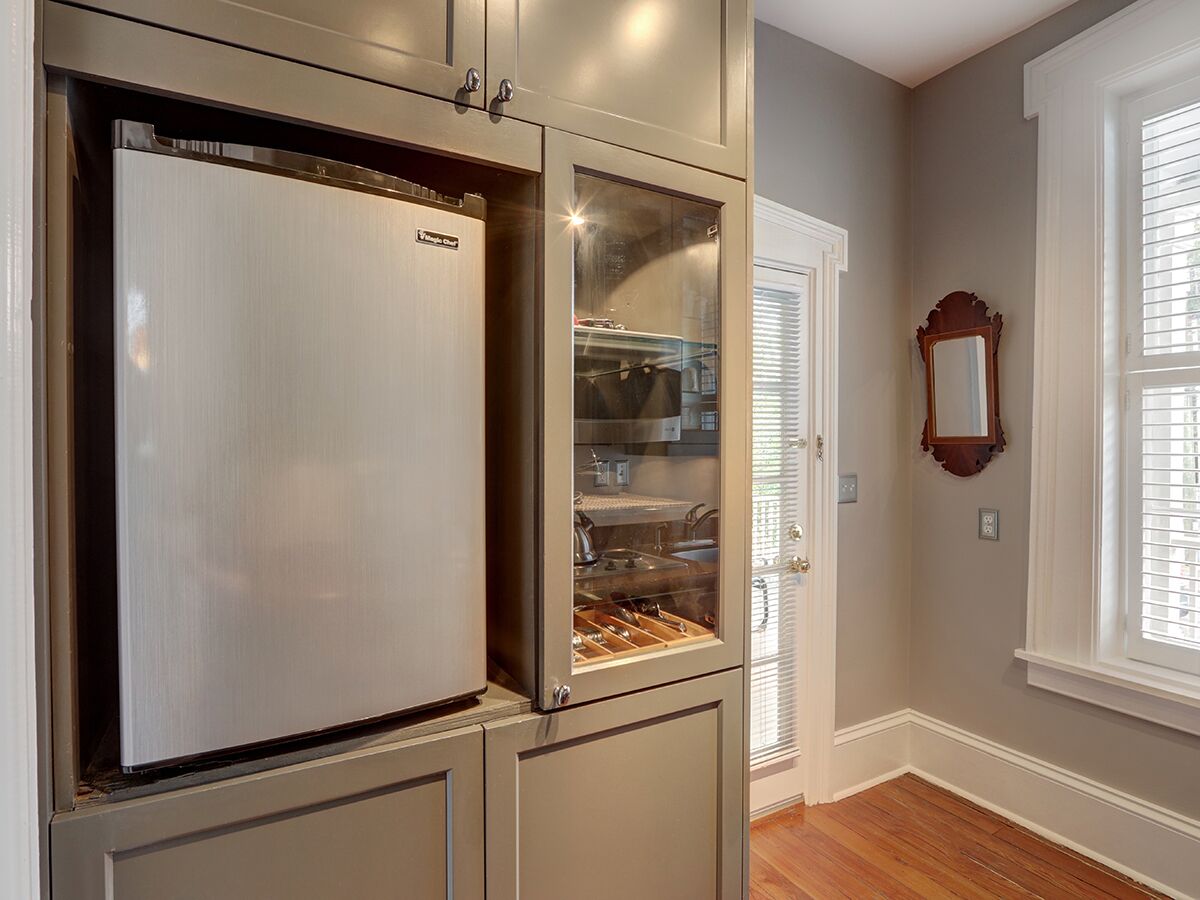 A kitchen with a stainless steel refrigerator, a glass-fronted pantry, and a wooden cabinet.