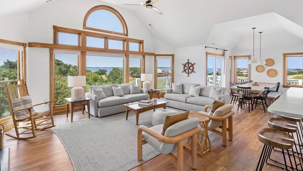 A spacious living area with large windows, a ceiling fan, and a dining area with a table and chairs. - Sound Decision: Hot Tub | Sound Views | Pool Access (Nags Head)