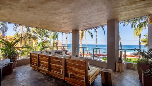 A wooden bench with cushions, large windows, and a view of the beach. - Casa Palmar 3BR  · Remarkable 3BR, 2BA Beachfront Condo (Sayulita)