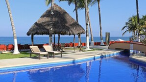 A pool area with lounge chairs, a thatched umbrella, and palm trees. - Casa Palmar 3BR  · Remarkable 3BR, 2BA Beachfront Condo (Sayulita)