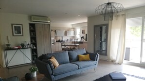 A modern living room with a sofa, a coffee table, and a rug. There is a kitchen in the background with a dining table and chairs. - Cocooning apartment 10 minutes from beaches (cabestany)