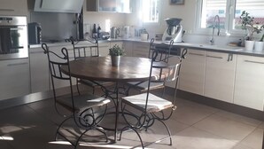 A modern kitchen with a dining table, chairs, and a window with blinds. - Cocooning apartment 10 minutes from beaches (cabestany)