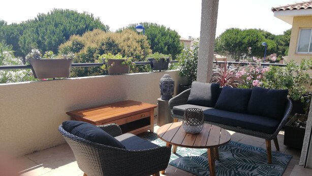 A balcony with wicker furniture, a Buddha statue, and potted plants. - Cocooning apartment 10 minutes from beaches (cabestany)