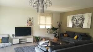 A modern living room with a grey sofa, a flat-screen TV on a white stand, a coffee table, and a large window with sheer curtains. - Cocooning apartment 10 minutes from beaches (cabestany)