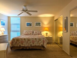 Une chambre à coucher avec un lit, un ventilateur de plafond, une table de chevet avec une lampe et des tableaux encadrés accrochés au mur.