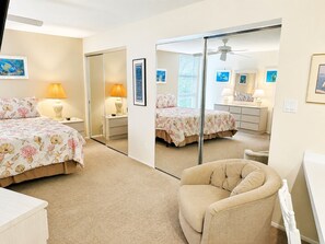 A bedroom with a bed, a chair, a dresser, a mirror, and a ceiling fan.