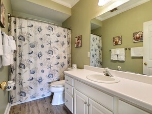 A bathroom with a shower curtain featuring a bird and sea shell pattern, a toilet, a sink with a mirror above it, and a door with a towel rack. - Heated Pool Access | 5*Clean | Flex Cancelation (Tybee Island)