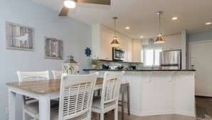 Una cucina moderna con mobili bianchi, un'isola centrale, illuminazione a sospensione e un'area pranzo con sedie bianche.