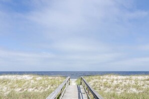 A wooden boardwalk leading to the beach with sand dunes on either side.