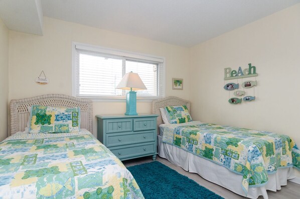A bedroom with two beds, a dresser, a window with blinds, and wall decorations.