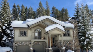 Una casa de dos pisos con fachada de piedra, un porche y un techo cubierto de nieve.