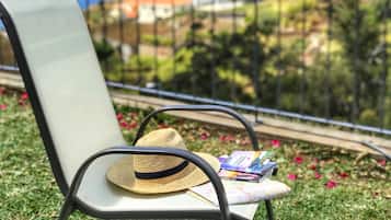 A chair with a straw hat and travel brochures on a grassy area with a view of a coastal landscape.