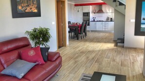 A modern living room with a red leather sofa, a dining area, and a kitchen with a staircase. - Modern Madeira house in Calheta, Madeira (Estreito da Calheta)
