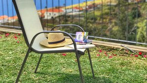 A chair with a straw hat and a book on a grassy area with a railing and a view of a town and hills in the background. - Modern Madeira house in Calheta, Madeira (Estreito da Calheta)