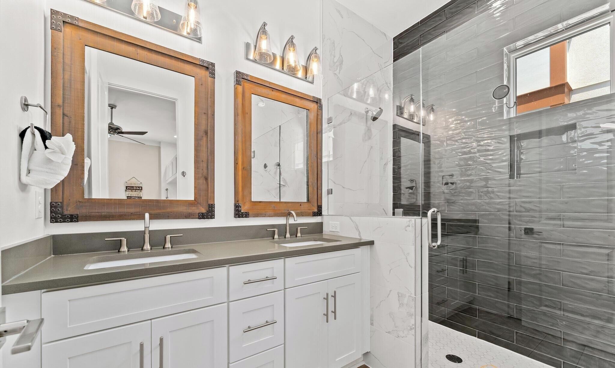 Een moderne badkamer met twee spiegels, een wastafel en een douche met glazen wanden.