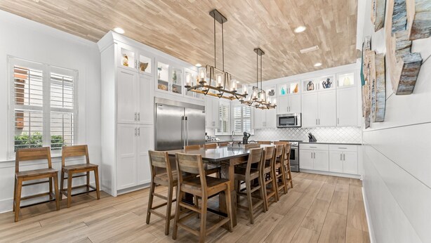 A modern kitchen with white cabinetry, a central island with wooden chairs, stainless steel appliances, and a wooden ceiling. - ☀️ Sol Experience | Golf Cart & Heated Community Pool | FREE Golf (Miramar)