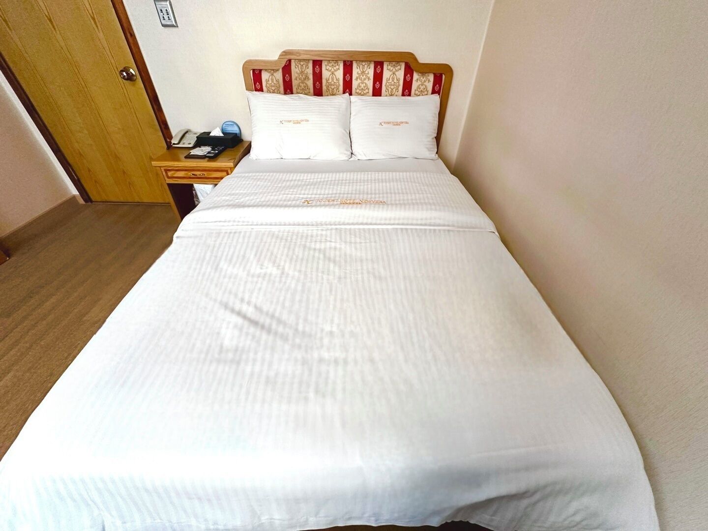 Una cama bien hecha con sábanas blancas y un cabecero a rayas.