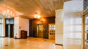A hotel lobby with a wooden ceiling, a chandelier, a reception desk, and a glass elevator. - Newvera Hotel (Cheongju)