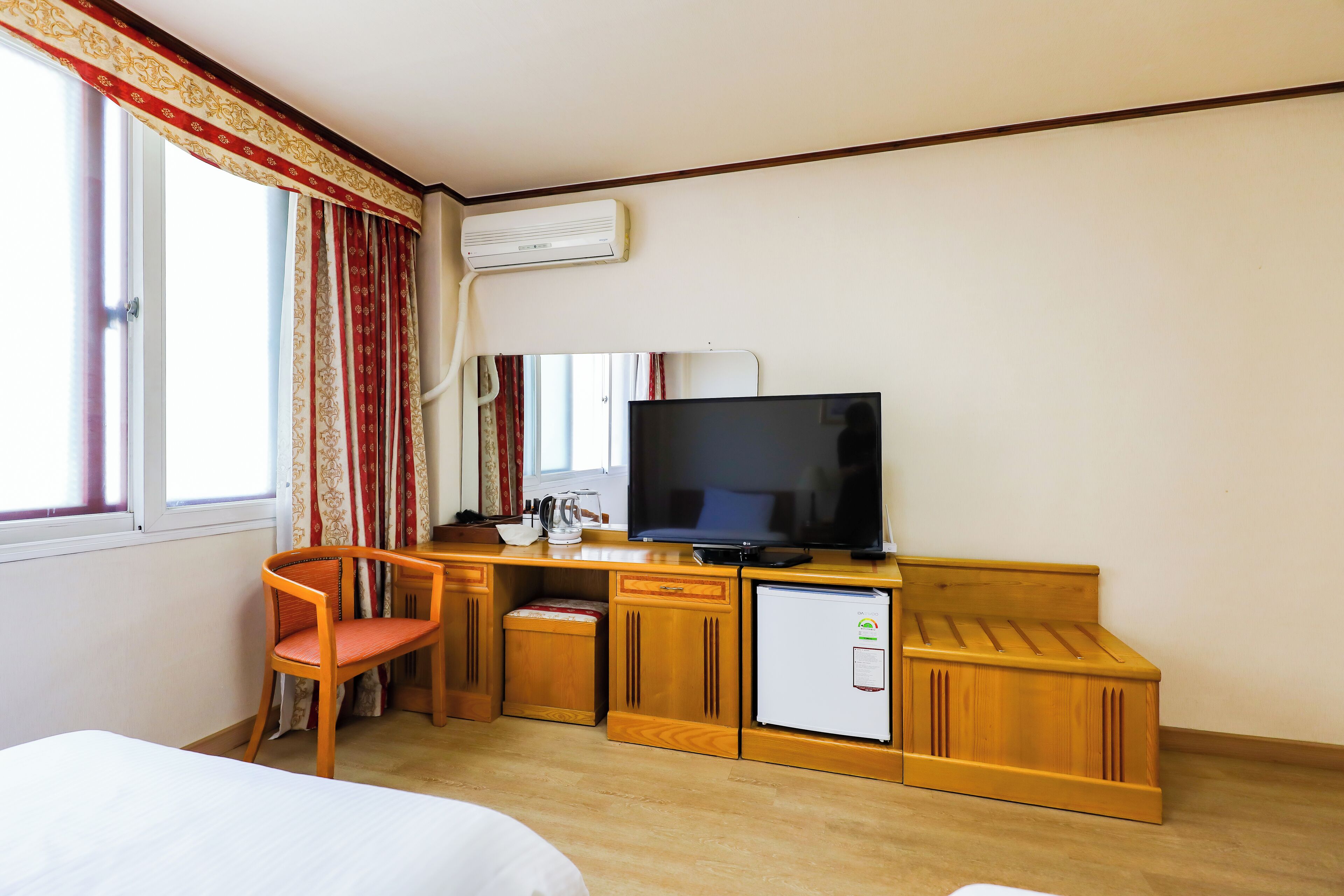 A hotel room with a bed, a desk with a television, a refrigerator, and a chair.