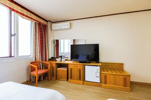 Una habitación de hotel con una cama, un escritorio con televisor, un refrigerador y una silla.