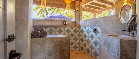 A bathroom with a large window, a towel rack, a sink, and a shower area.