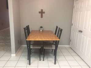 A dining table with four chairs, a cross on the wall, and a small plant on the table.