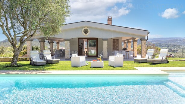 Une maison moderne avec une piscine, un espace salon extérieur et une vue sur les collines.