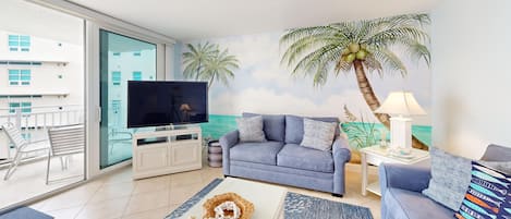 A living room with a sofa, a television, a coffee table, and a lamp. There is a balcony with a chair and a railing.
