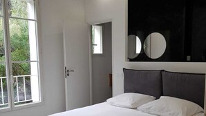 Un dormitorio moderno con una cama grande, un ventanal con vistas a zonas verdes y un cabecero oscuro con espejo.