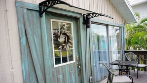 A wooden door with a frosted glass window, a metal sign above it, and a patio with a table and chairs. - Fall Specials Available! Pet Friendly! Steps to white sandy beaches and the bay!  Discounts applied for stays longer than 7 days and 30 days! (Bradenton Beach)