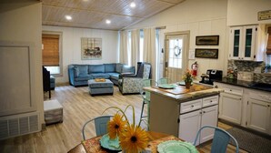 A spacious living area with a sofa, ottoman, and chairs, a kitchen with white cabinets, and a dining area with a table and chairs. - Fall Specials Available! Pet Friendly! Steps to white sandy beaches and the bay!  Discounts applied for stays longer than 7 days and 30 days! (Bradenton Beach)