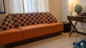 Ein Zimmer mit einer Couch, einem Schreibtisch mit Lampe und Globus sowie einem Fenster mit Vorhängen.