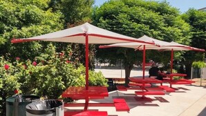 Sitzbereich im Freien mit Tischen und Sonnenschirmen, umgeben von viel Grün.