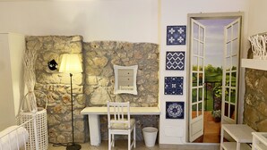 A small, cozy room with a stone wall, a white desk, a chair, a lamp, and a view of a garden through a door. - Circeii, apartment with bedroom, living room and exterior with bathtub (San Felice Circeo)