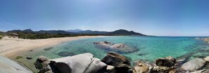 A coastal landscape with clear turquoise waters, rocky shoreline, and distant mountains.