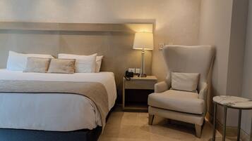 A hotel room with a large bed, a nightstand with a lamp, a chair, and a small table.