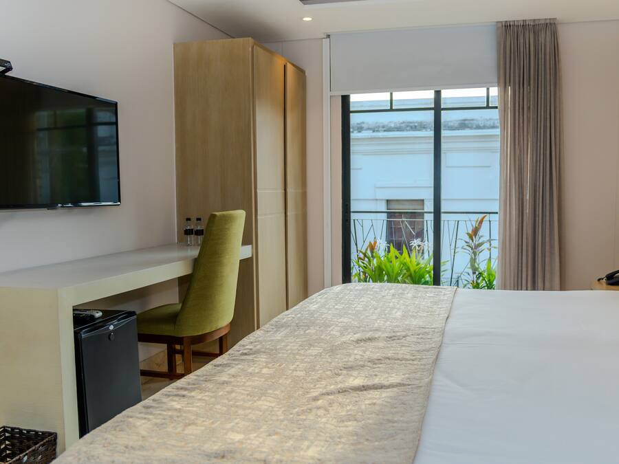 A hotel room with a bed, a desk, a chair, a TV, a balcony with a view of the water, and a phone on the nightstand.