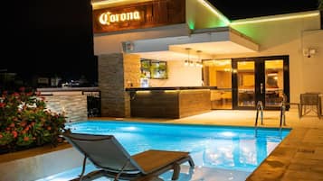 Vista nocturna de un hotel con piscina, zona de bar y restaurante.