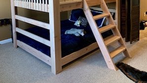 Letto a castello con struttura in legno, scaletta, una piccola finestra e una porta.