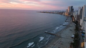 Un paysage urbain côtier avec une plage, des immeubles de grande hauteur et une mer calme au coucher du soleil.