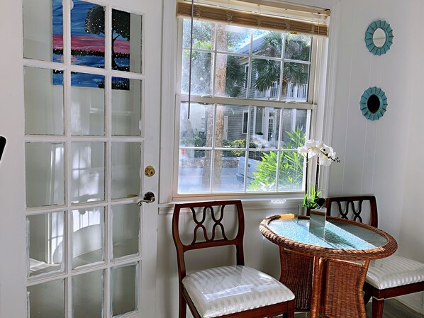 A room with a large window, a wicker table, two chairs, and a door with frosted glass panels.