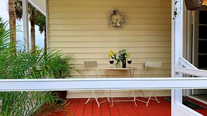 Une terrasse en bois rouge avec une balustrade blanche, une table avec des chaises et une couronne décorative accrochée au mur.
