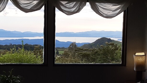 A room with a large window offering a view of mountains and a lake. - MONTEVERDE - Comfy, well-equipped House in woods with spectacular view! (Santa Elena)