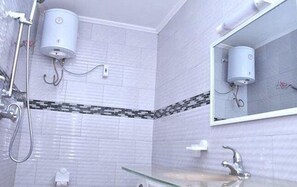 A bathroom with white tiled walls, a glass shower enclosure, a mirror, and a white toilet.