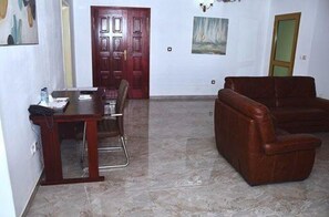 A room with a dining table, chairs, a brown leather sofa, and a door.