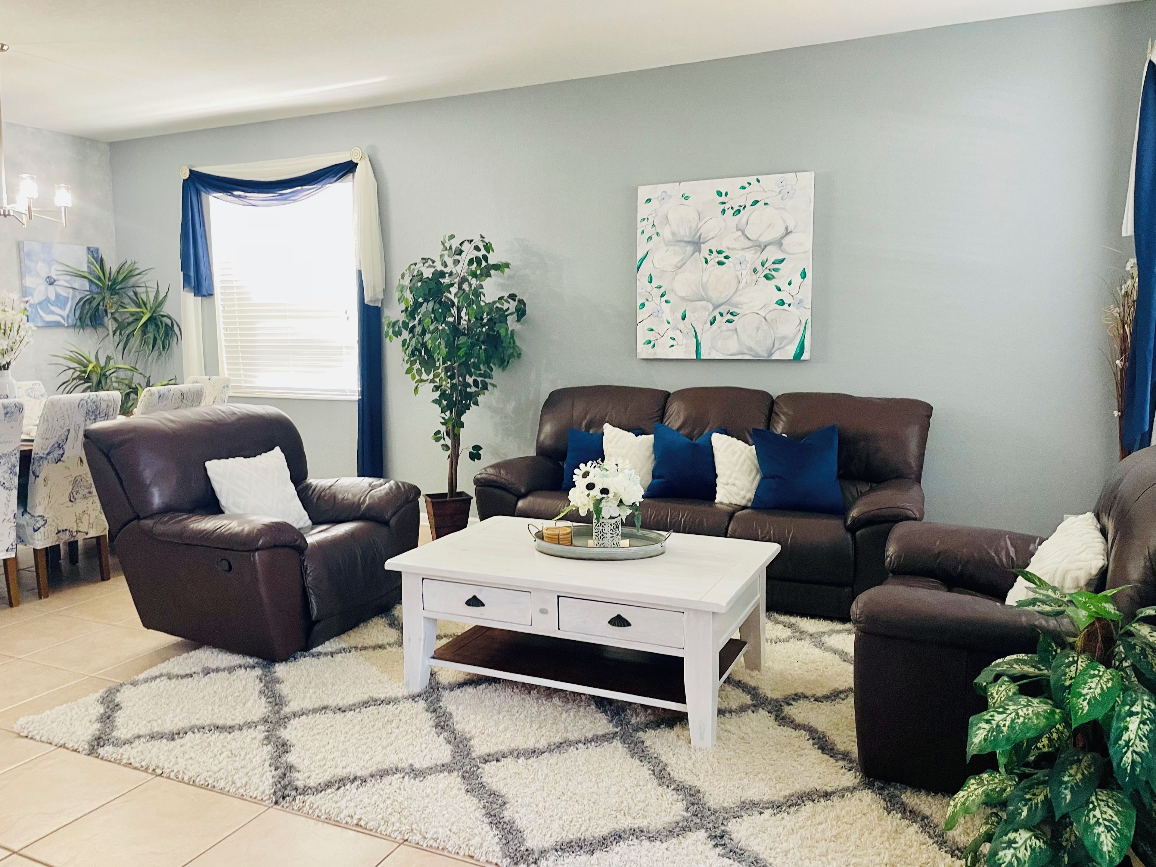 A living room with a brown leather sofa, a white coffee table, and a blue and white abstract painting on the wall.