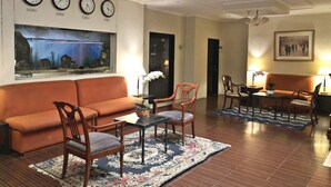 A hotel lobby with a sofa, chairs, a coffee table, a fish tank, clocks, and a painting. - Royale Tagaytay B&B (Alfonso)