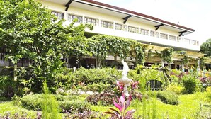 A garden with a statue, lush greenery, and a building with a balcony in the background. - Royale Tagaytay B&B (Alfonso)