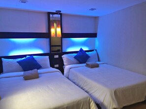 A hotel room with two beds, each with white bedding and blue pillows. There is a large mirror above the beds, and the room has a modern design with blue lighting accents. - Royale Tagaytay B&B (Alfonso)
